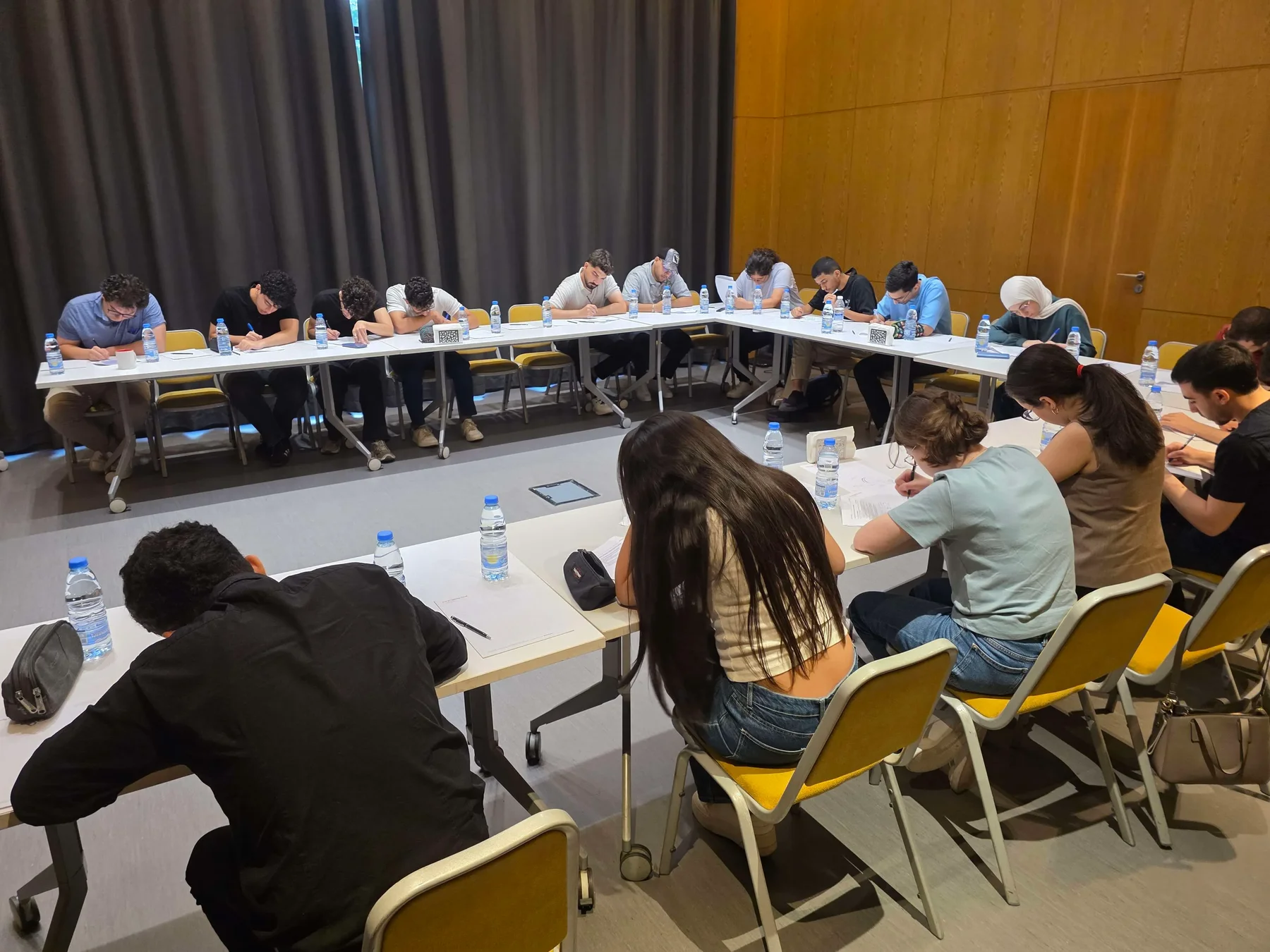 Students seated at U-shaped conference tables writing their midterm exams in a hotel conference room